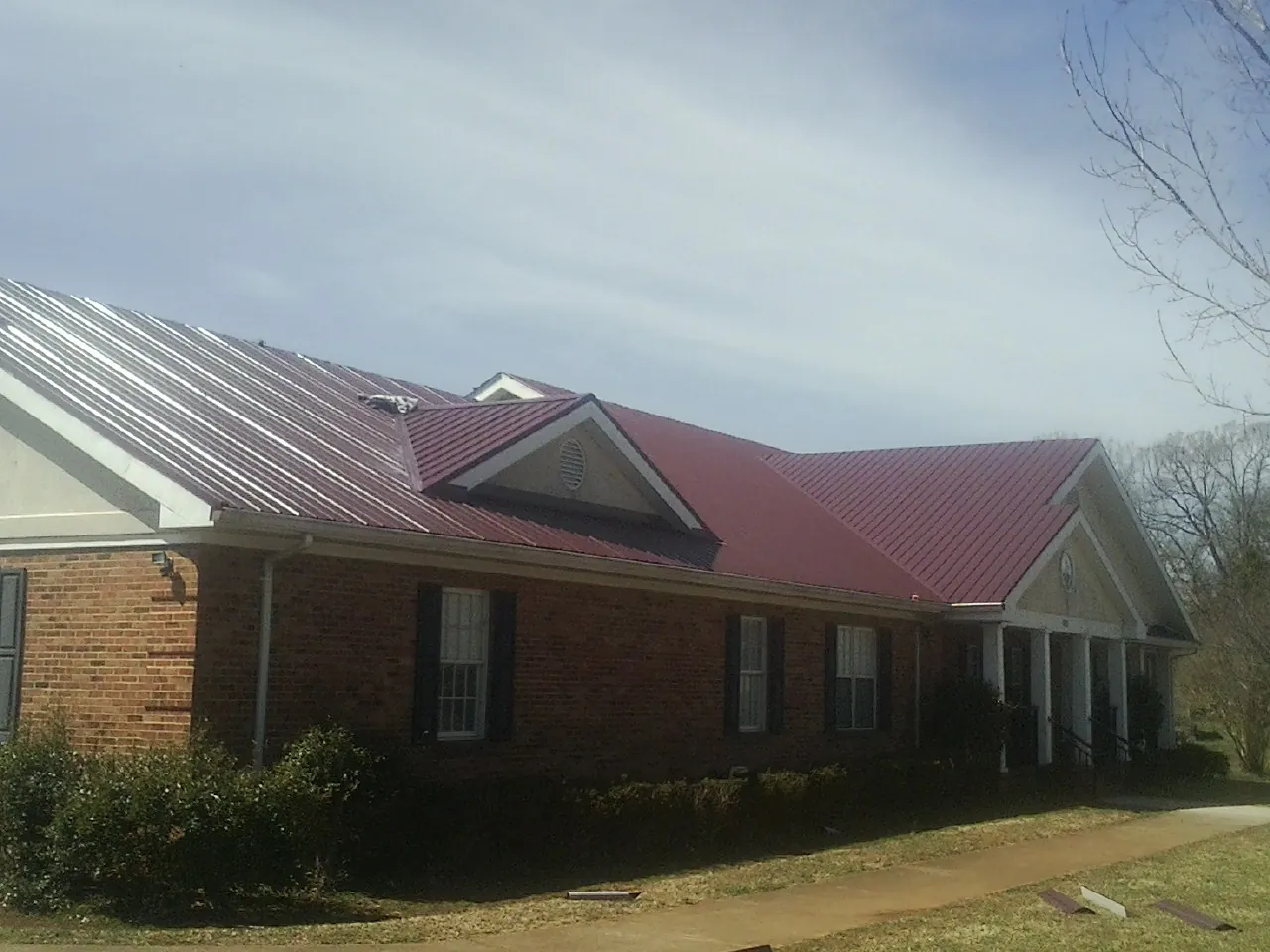 Red metal roof with gabled entries on a long brick building, from a Hail Damage Roof Repair job in Cherokee