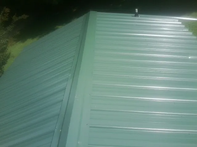 New green metal panels meeting at the ridge of a roof — Flat Roof Repair work by our crew in Cherokee