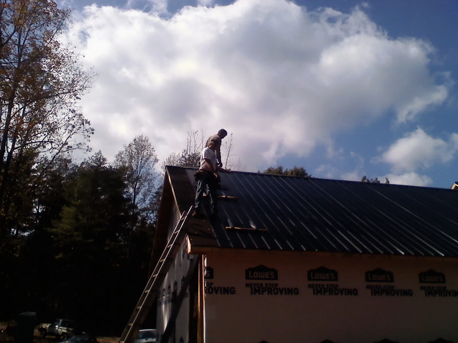 Roofer fastening dark metal panels high against a cloudy sky, from a Roof Inspection job in Cherokee